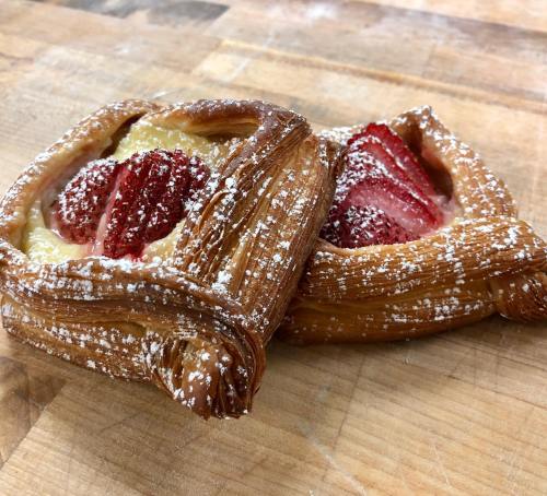 Two flaky pastries filled with cream and topped with fresh strawberries, dusted with powdered sugar on a wooden surface.