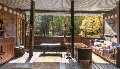Cozy screened porch with wooden decor, a sofa, and views of a forested area with autumn foliage.