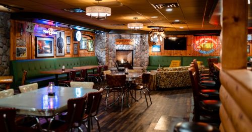 Cozy restaurant interior with wooden walls, stone fireplace, and various seating options, creating a warm atmosphere.