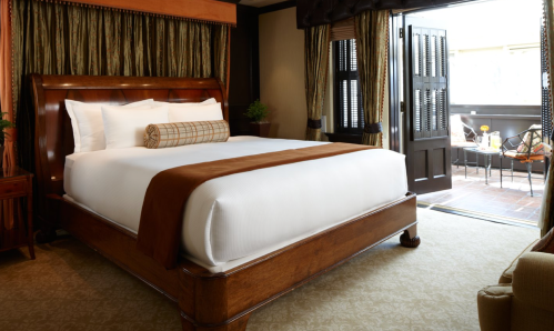 A cozy hotel room featuring a large bed with a brown throw, elegant decor, and a balcony door leading outside.