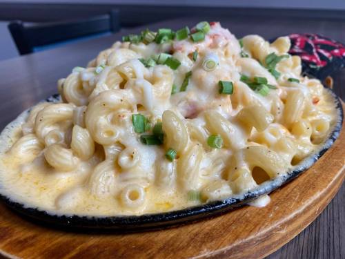 Creamy macaroni and cheese topped with green onions, served in a sizzling skillet on a wooden board.