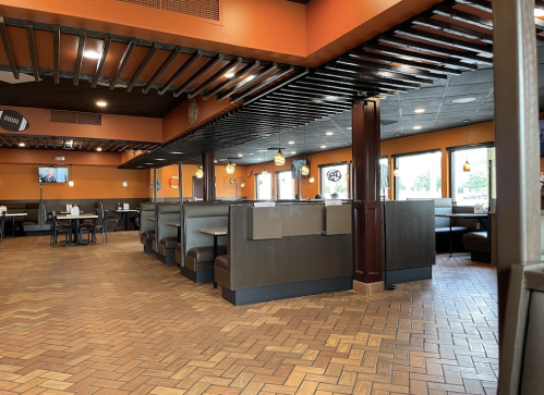 Interior of a restaurant featuring orange walls, booths, and a wooden ceiling with a tiled floor.