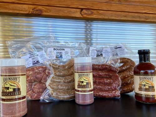 Assorted sausages and seasonings from Johnson's Boucanière, including boudin and BBQ sauce on a black surface.