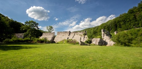Lush green landscape with rocky cliffs under a blue sky with scattered clouds.