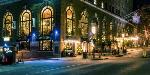A beautifully lit brick building with arched windows, decorated for the holidays, along a quiet street at night.