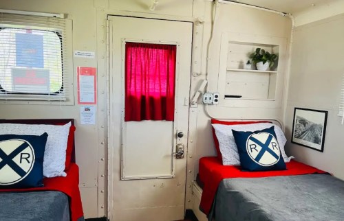 Cozy interior of a train-themed room with two beds, red accents, and a door with a red curtain.
