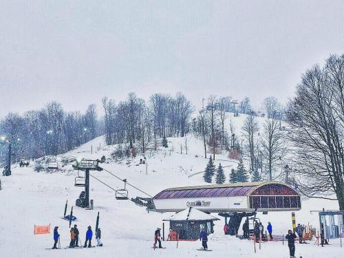 Ski resort scene with a chairlift, snowy slopes, and skiers preparing to ride in a winter landscape.