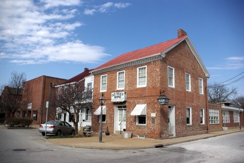 Historic brick building with a red roof, featuring white awnings and a sign, set against a blue sky.