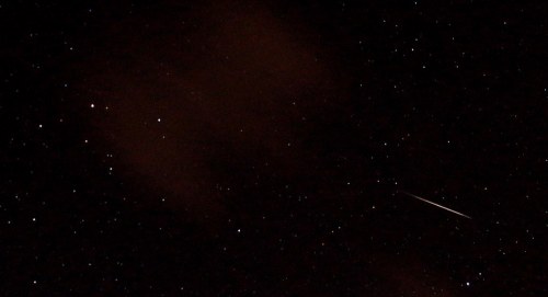 A night sky filled with stars, featuring a bright meteor streaking across the scene.