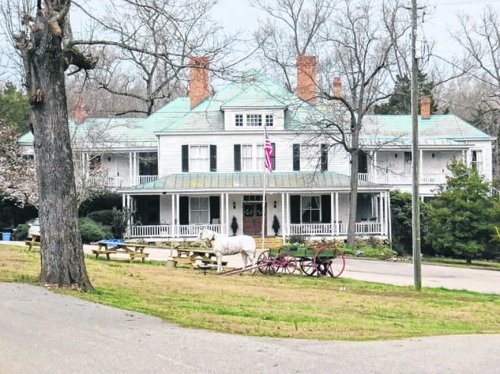 A large, historic white house with a green roof, surrounded by trees and a horse-drawn carriage in the foreground.
