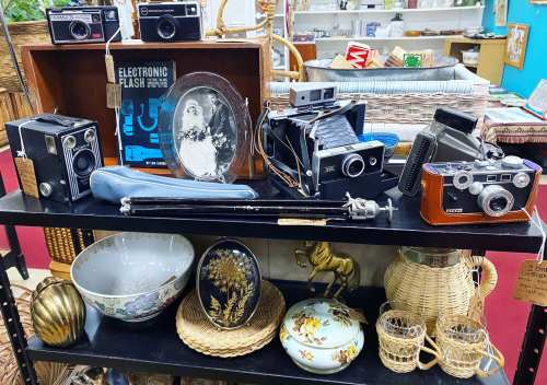 A display of vintage cameras, a framed photo, and various decorative items on a black shelf in a thrift store.