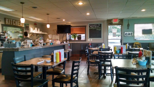 Cozy diner interior with tables, condiments, and a kitchen area; welcoming atmosphere with a chalkboard sign.