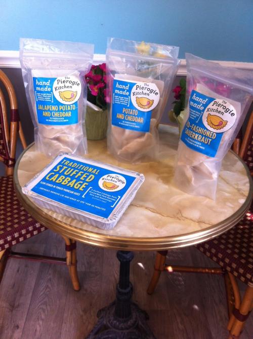 Three bags of pierogies and a tray of stuffed cabbage on a round table with a checkered chair.