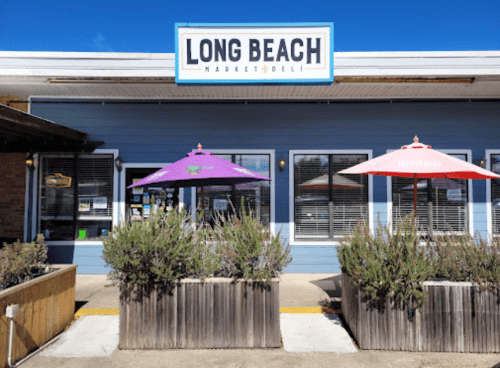 Exterior of Long Beach Market & Deli with purple and red umbrellas on a sunny day.