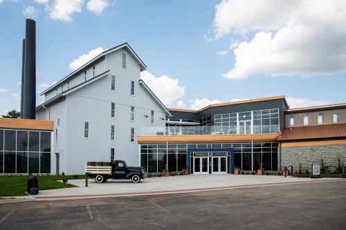A modern building with large windows, a vintage truck in front, and a blue sky with clouds above.
