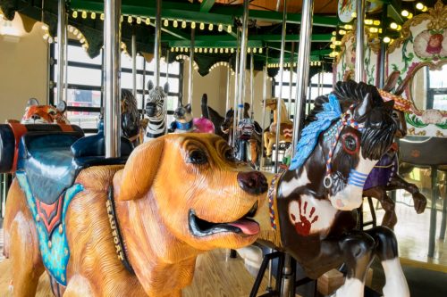 A colorful carousel featuring a large dog and a horse, surrounded by various animal figures and bright lights.