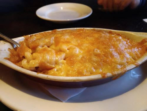 A baked dish of macaroni and cheese with a golden, crispy cheese topping in a white serving bowl.