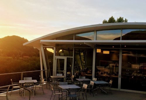 Modern restaurant exterior with outdoor seating, surrounded by mountains and a sunset sky.