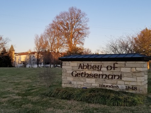 Sign for the Abbey of Gethsemani, established in 1848, with trees and a building in the background during sunset.