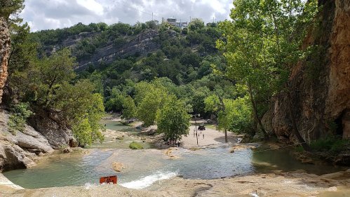 A scenic view of a river flowing through rocky terrain, surrounded by lush greenery and distant hills.
