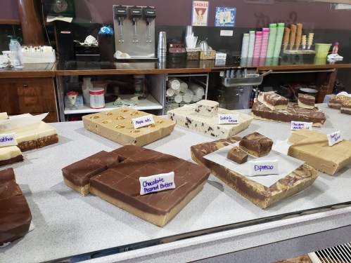 A display case filled with various fudge flavors, including chocolate peanut butter and espresso, in a candy shop.