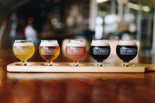 A wooden flight board holds five small glasses of different craft beers, each labeled with "Iron Bridge."