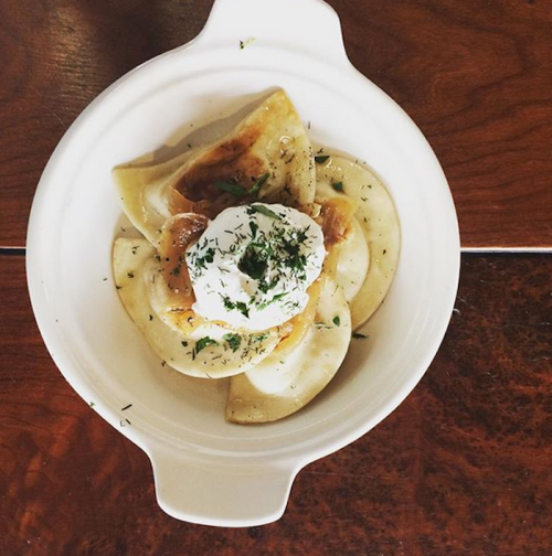 A bowl of dumplings topped with sour cream and herbs, served on a wooden table.