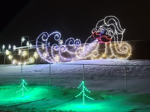 Colorful holiday lights depict a whimsical Santa in a sleigh, surrounded by snow and festive trees at night.