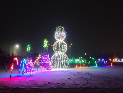 A large illuminated snowman stands among colorful holiday lights in a snowy landscape at night.