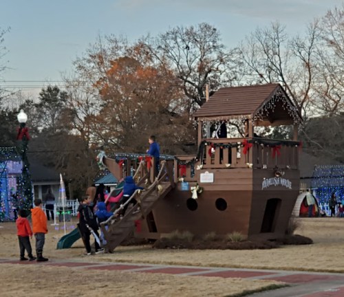 A wooden play structure resembling a ship, decorated for the holidays, with children playing and adults nearby.