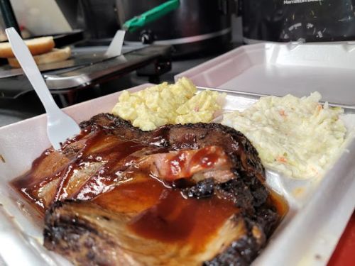 A plate of barbecue brisket with sauce, served alongside creamy coleslaw and potato salad.