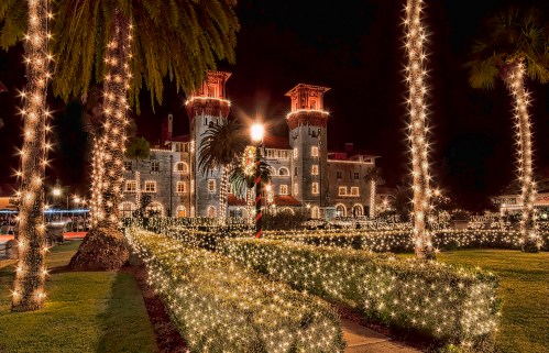 A beautifully lit historic building surrounded by palm trees and festive lights at night.