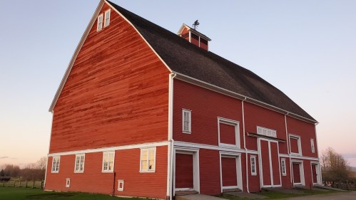 A large red barn with a peaked roof and white trim, set against a soft evening sky.
