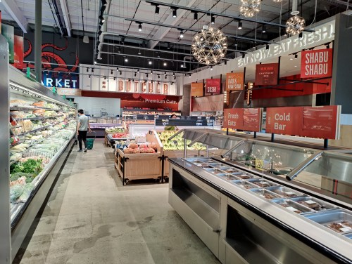 A spacious grocery store interior featuring fresh produce, a butcher section, and a cold bar display.