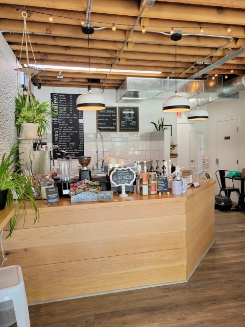 A cozy coffee shop interior featuring a wooden counter, hanging lights, and a menu board with plants in the background.