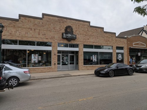 A brick building with large windows, featuring a sign that reads "Lion Bridge," and parked cars in front.