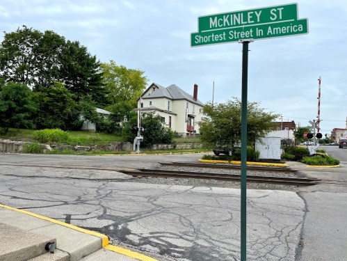 Sign for McKinley St, labeled as the shortest street in America, with a residential area and railroad tracks nearby.