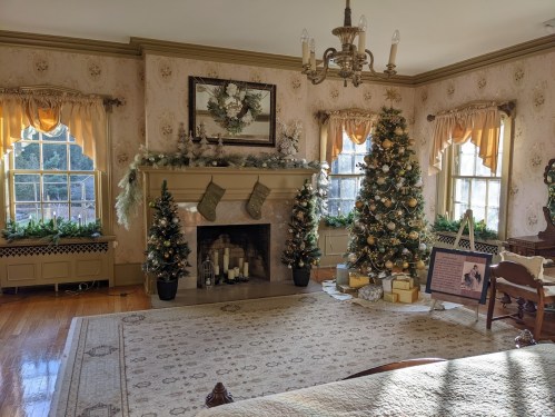 Cozy living room decorated for the holidays, featuring two Christmas trees, stockings, and festive garlands.