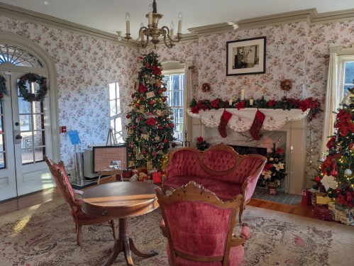 Cozy room decorated for the holidays, featuring a Christmas tree, floral wallpaper, and a fireplace adorned with stockings.