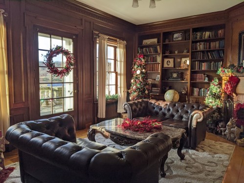 Cozy living room decorated for the holidays, featuring a Christmas tree, wreaths, and elegant furniture.