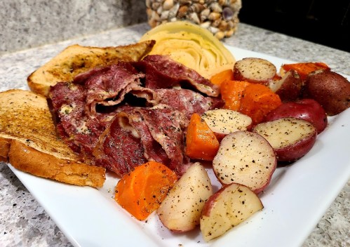 A plate of corned beef, toast, cheese, and seasoned roasted potatoes and carrots on a granite countertop.