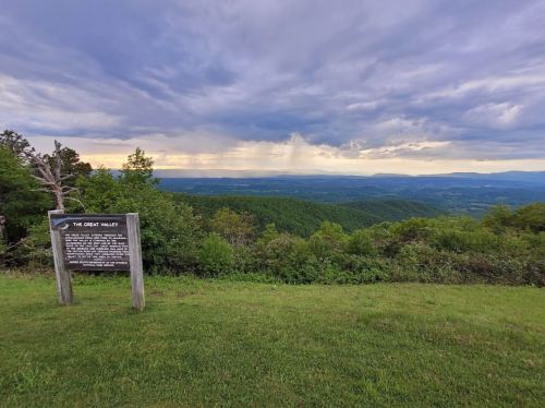 A scenic view of a valley under a cloudy sky, with a sign in the foreground providing information about the area.