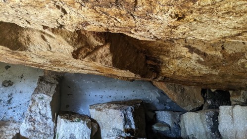 Interior of a cave with large, uneven rock formations and a textured ceiling. Natural light illuminates the space.