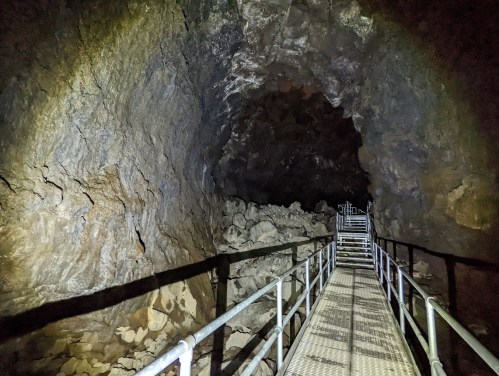 A dimly lit cave interior with a metal walkway leading through rocky terrain.
