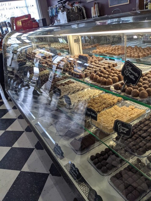 A display case filled with various confections, including chocolates and fudge, in a cozy shop setting.