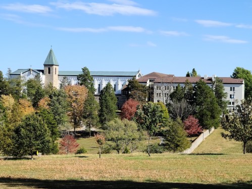 A scenic view of a large building complex surrounded by trees with autumn foliage under a clear blue sky.
