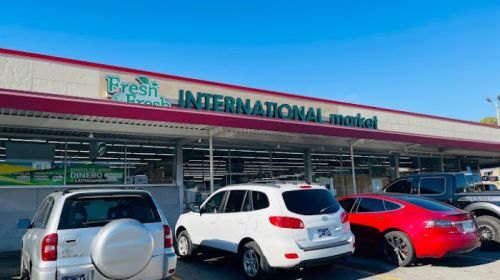 Exterior of an international market with a bright blue sky, featuring parked cars in front.