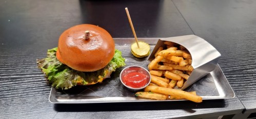 A burger with lettuce on a plate, accompanied by a small container of fries and a side of ketchup.