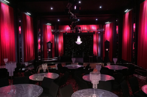 Elegant theater interior with red curtains, a chandelier, and round tables set for an event.