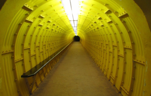 A long, brightly lit yellow tunnel with a smooth floor and a dark exit at the end.
